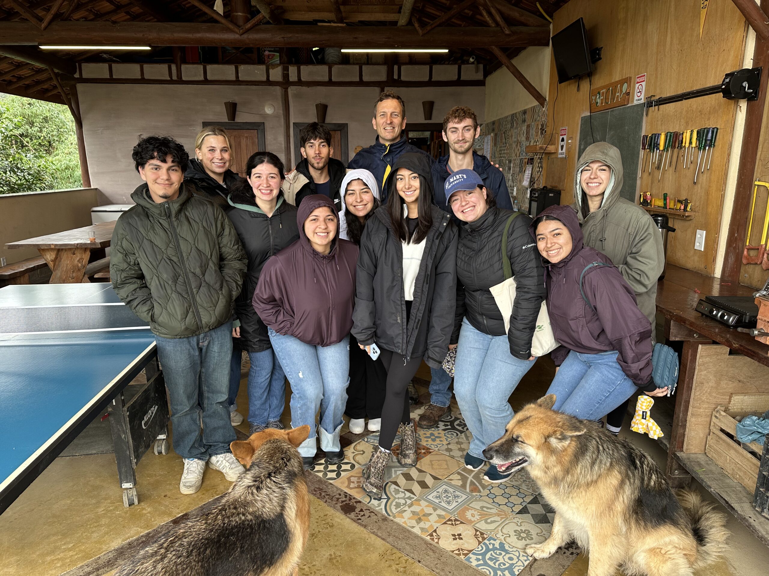 A group of young people and staff members posing together indoors near a table, with a dog sitting in the foreground.A group of young people and staff members posing together indoors near a table, with a dog sitting in the foreground.